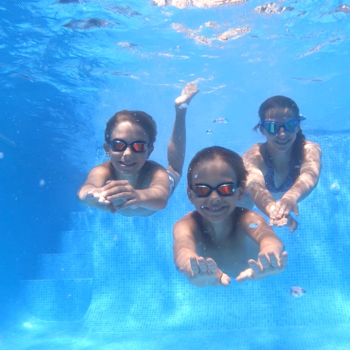 Three smiling campers swimming underwater in a swimming pool